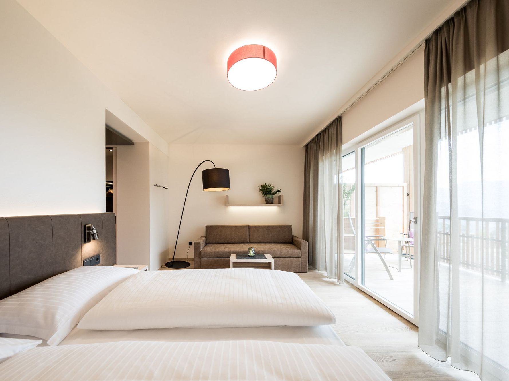Modernes Hotelzimmer mit Bett, Sofa, Stehlampe und großer Fensterfront