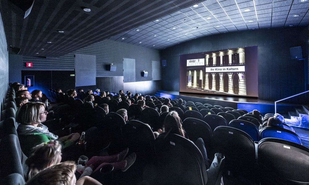 Ein Kino mit Zuschauern, die einen Film auf einer großen Leinwand sehen.