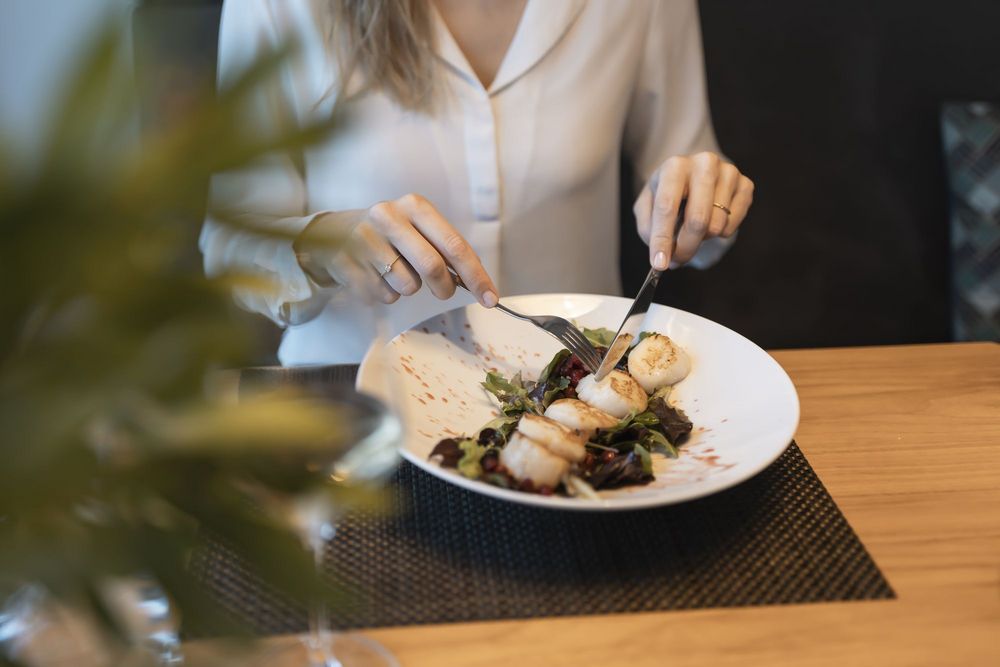 Person schneidet Jakobsmuscheln auf einem Teller mit Salat
