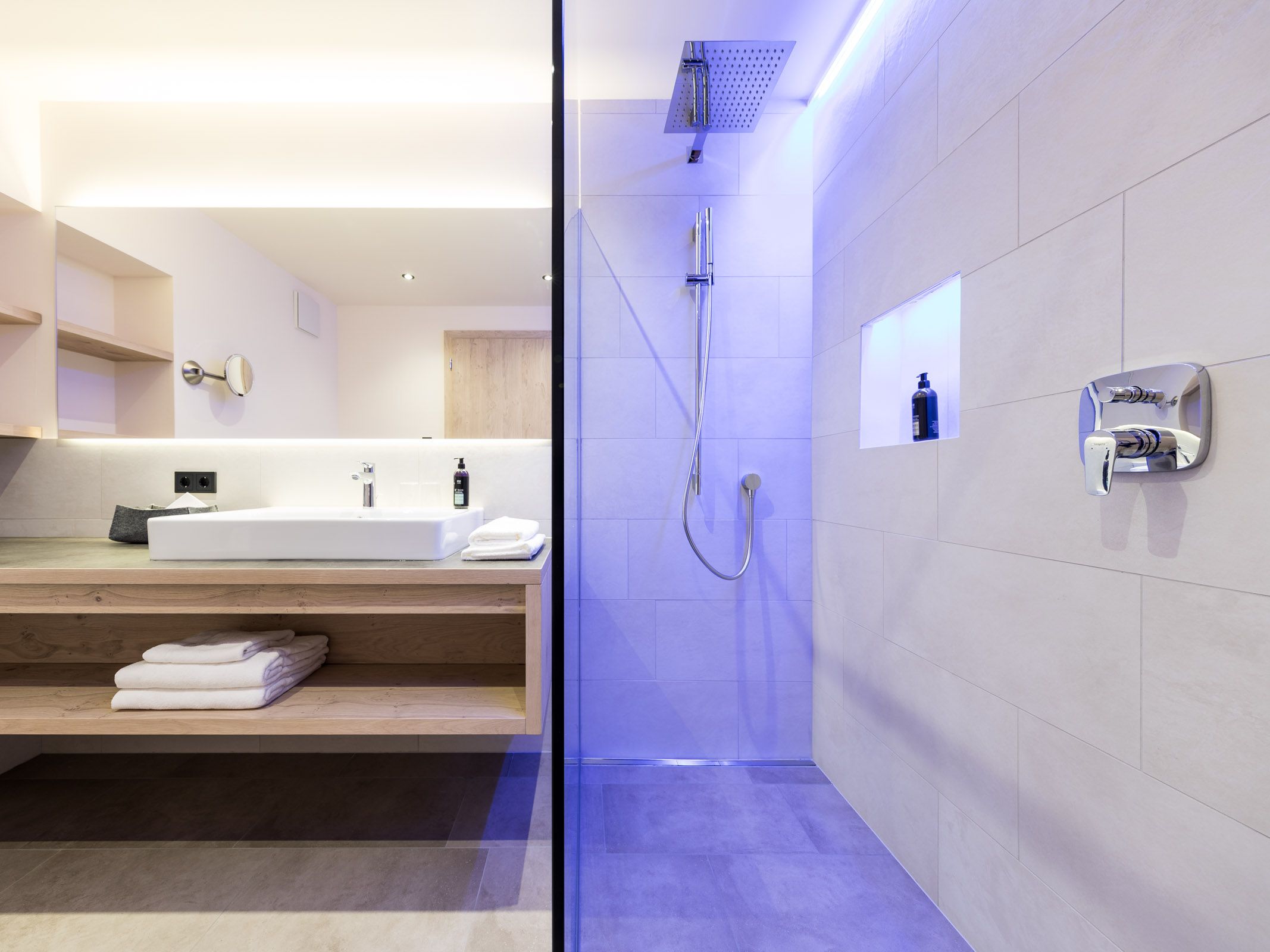 Modernes Badezimmer mit Holzwaschtisch und begehbarer Dusche mit blauer Beleuchtung