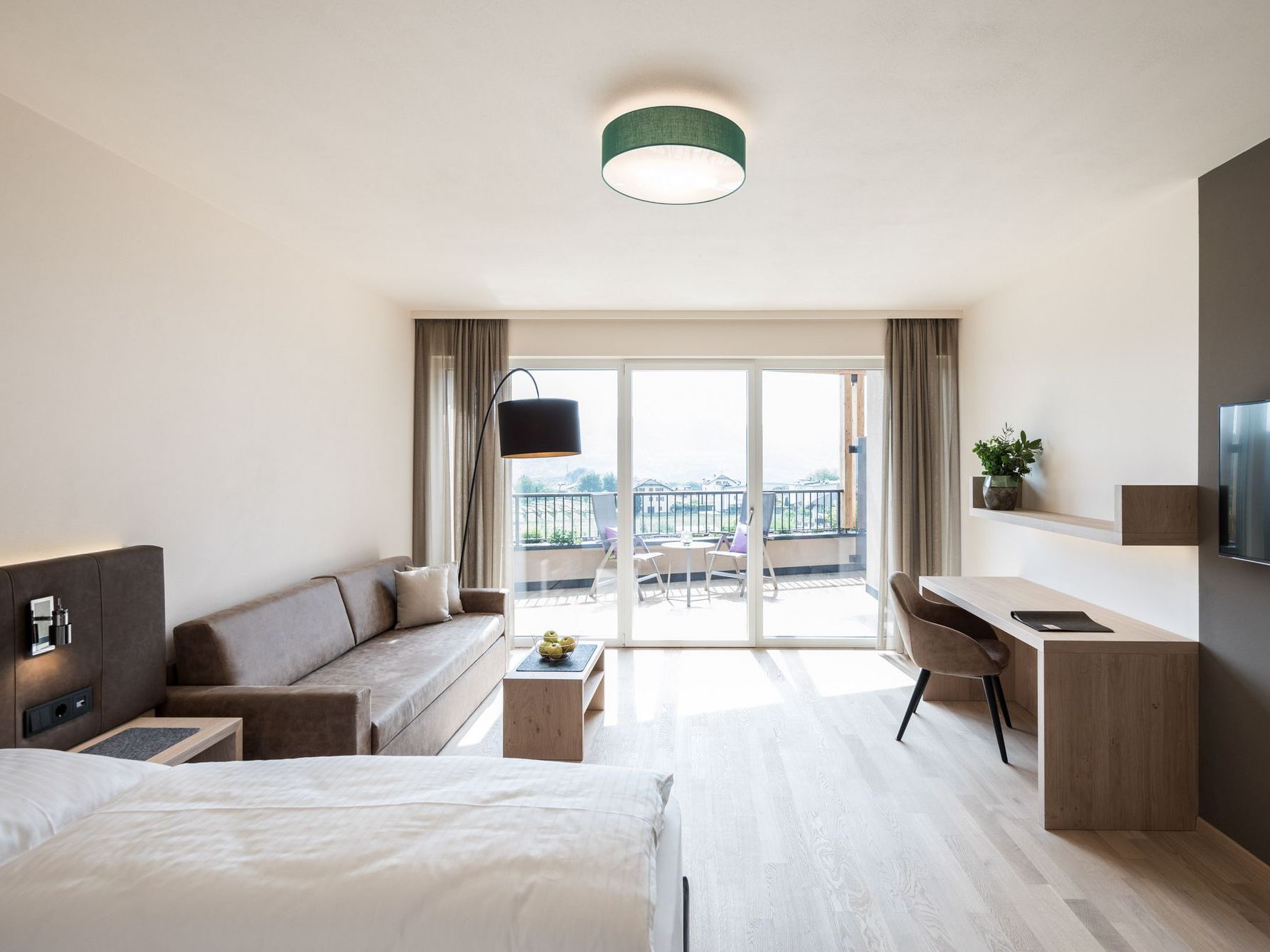 Helles Hotelzimmer mit Bett, Sofa, Schreibtisch und Balkonblick