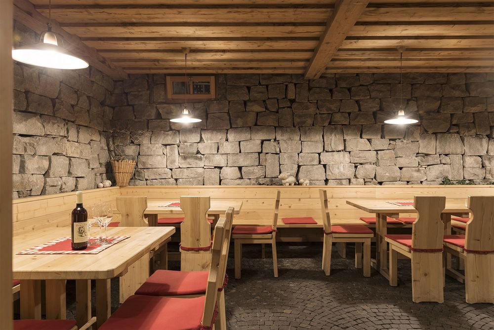 Rustikaler Gastraum mit Holzmöbeln, roten Sitzkissen und Steinmauerwand