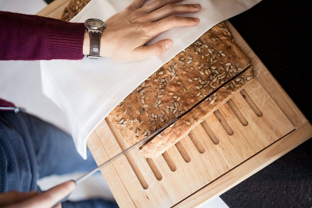 Person schneidet Sonnenblumenkernbrot auf einem Holzbrett