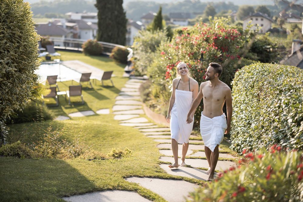 Paar geht barfuß in Badetüchern auf einem Gartenweg entlang