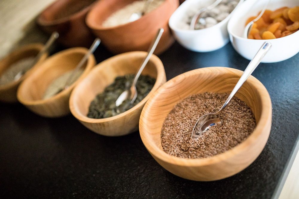 Verschiedene Samen und getrocknete Früchte in Schalen mit Löffeln auf einem schwarzen Tisch