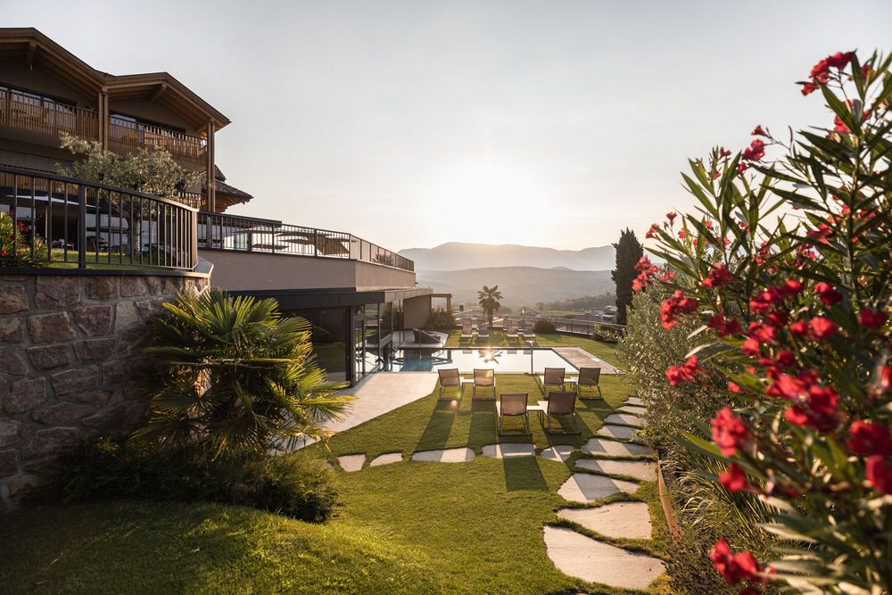 Sonnenuntergang über Garten mit Liegestühlen und Pool neben modernem Haus und roten Blumen.