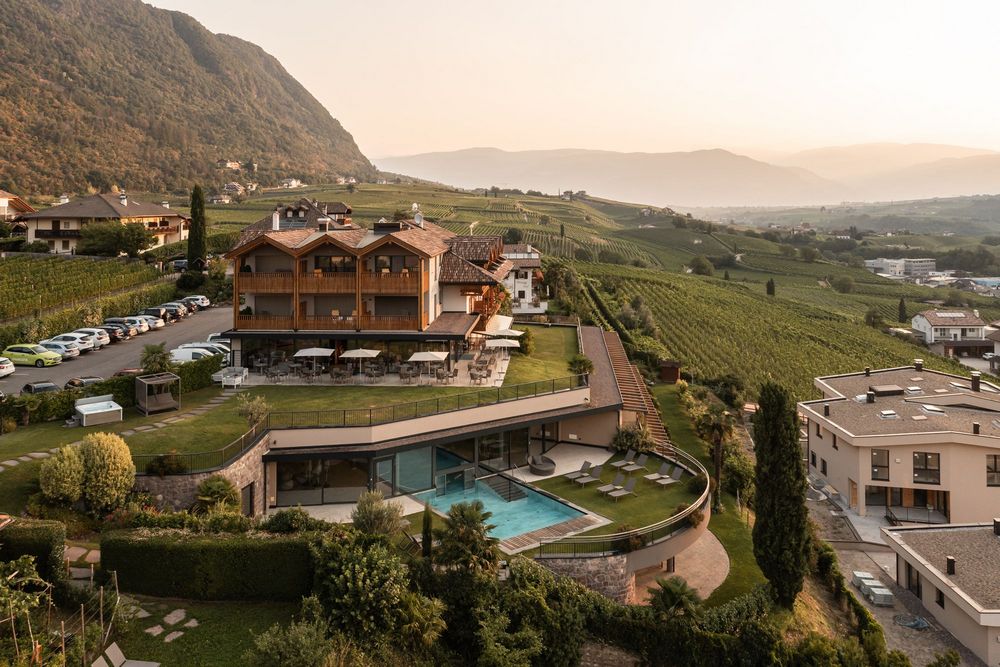 Modern hotel with outdoor pool surrounded by vineyards and mountains at sunset.
