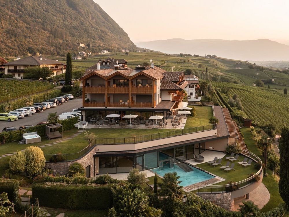 Hotel mit Außenpool und Liegestühlen in einer grünen Hügellandschaft bei Sonnenuntergang.