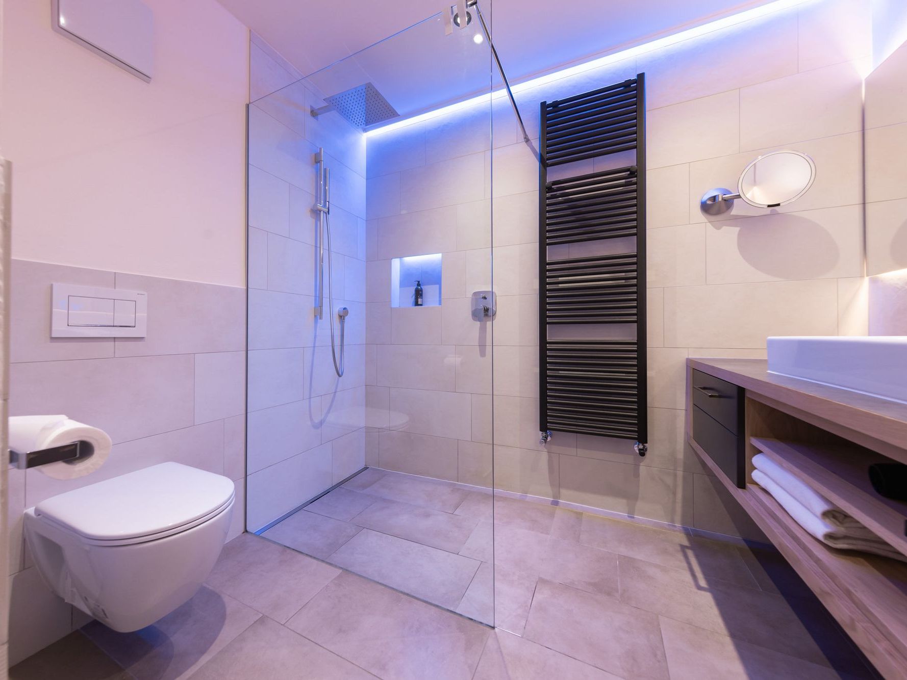 Moderner Badezimmer mit Dusche, Hänge-WC und beleuchtetem Spiegel.