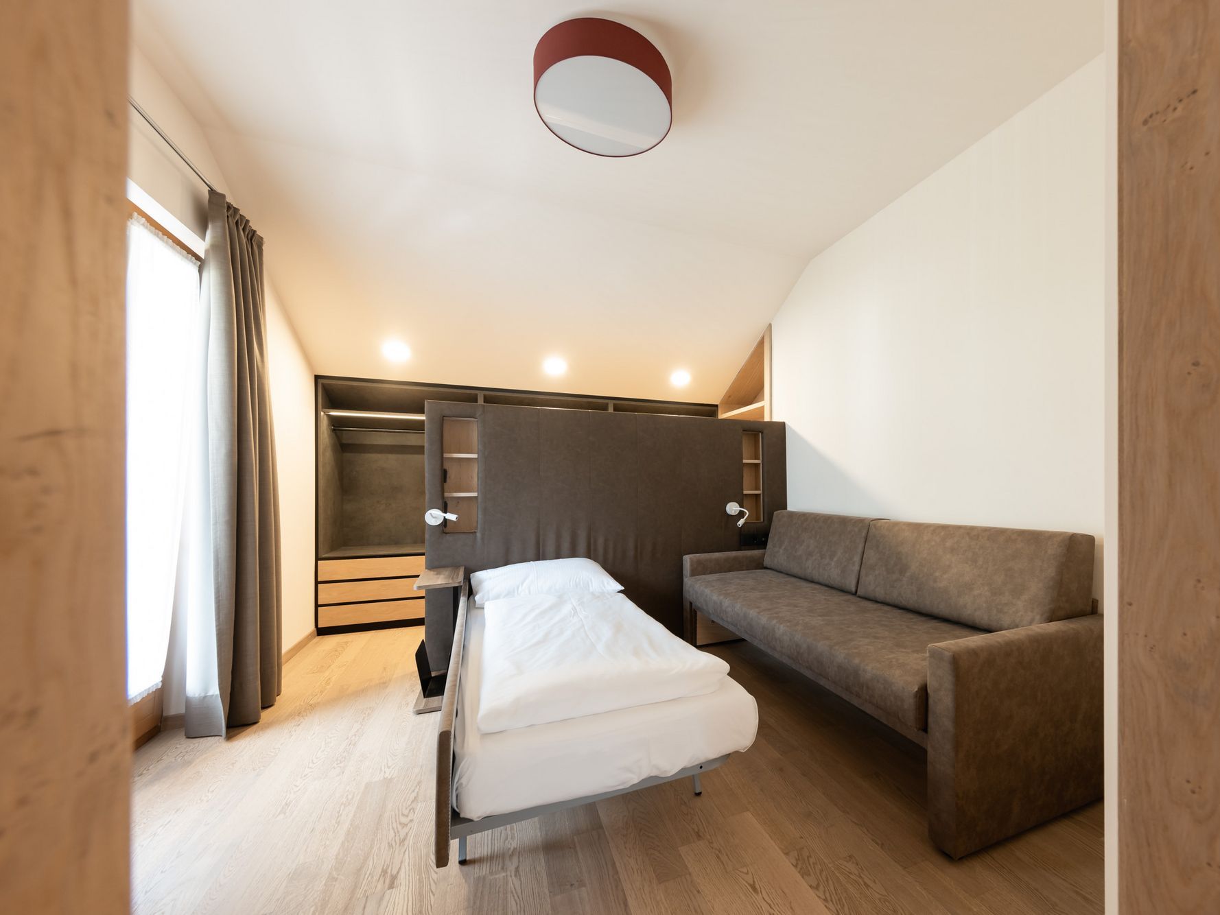 Kleines, modernes Schlafzimmer mit ausklappbarem Einzelbett und brauner Couch.