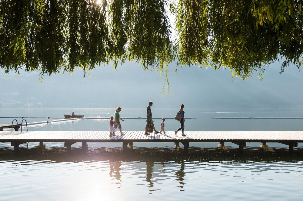 Familie geht auf einem Steg am See unter grünen Ästen spazieren