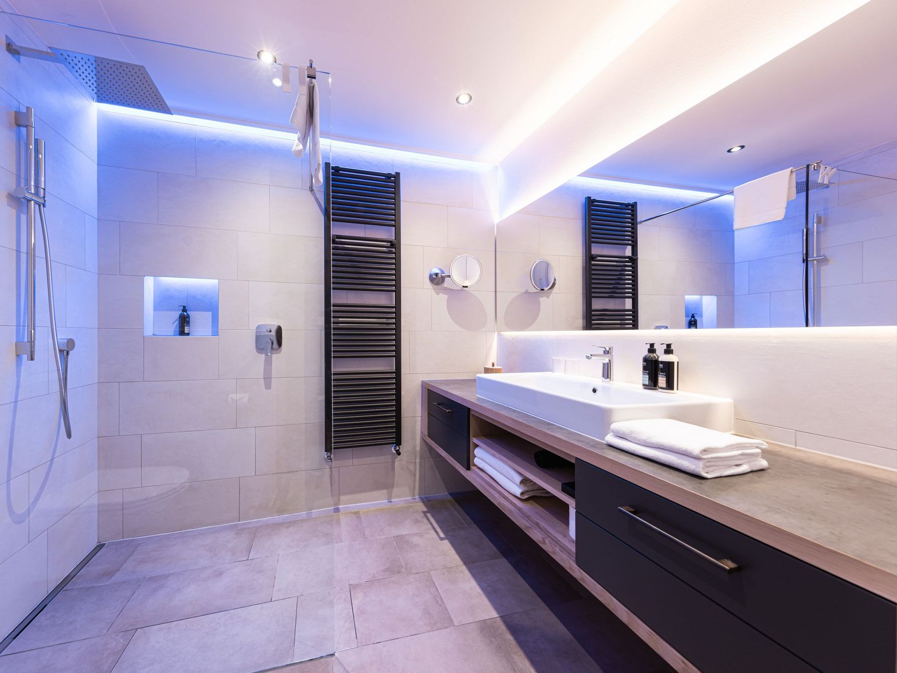 Modernes Badezimmer mit großer Dusche, Waschtisch und indirekter blauer Beleuchtung