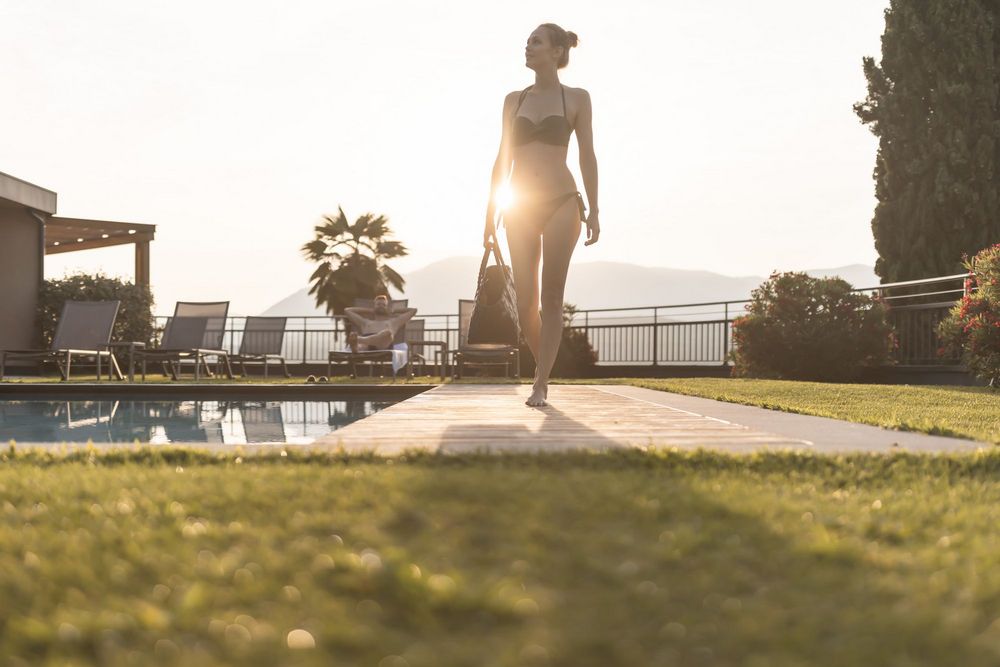 Frau im Bikini geht am Pool entlang bei Sonnenuntergang