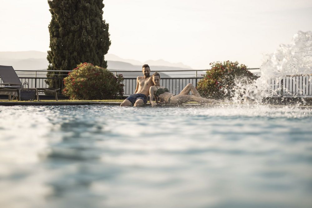 Paare entspannen am Beckenrand eines Pools bei Sonnenuntergang.