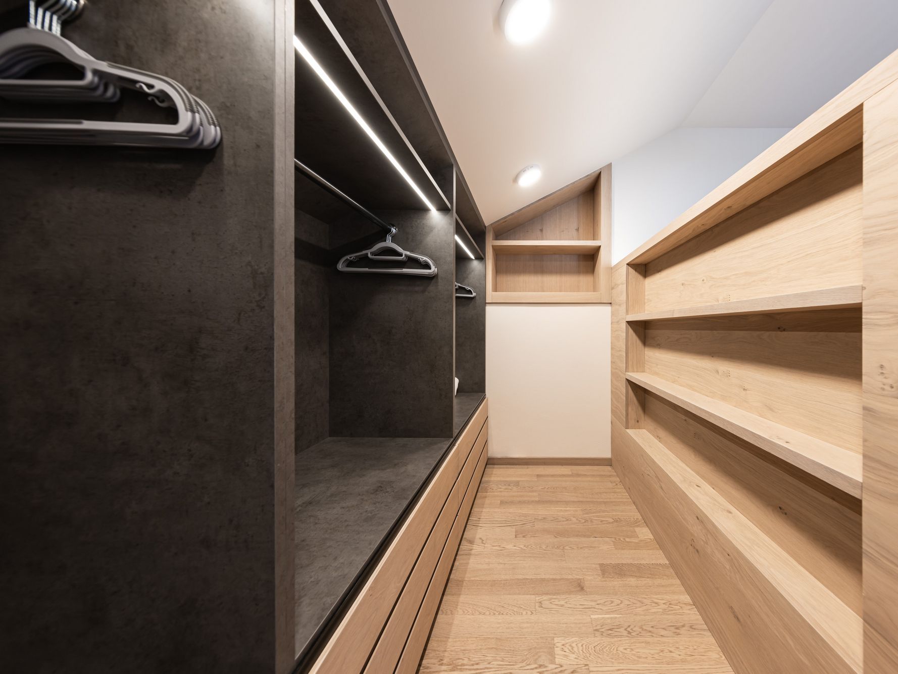 Moderner begehbarer Kleiderschrank mit Holzregalen und dunklen Fächern mit Kleiderbügeln.