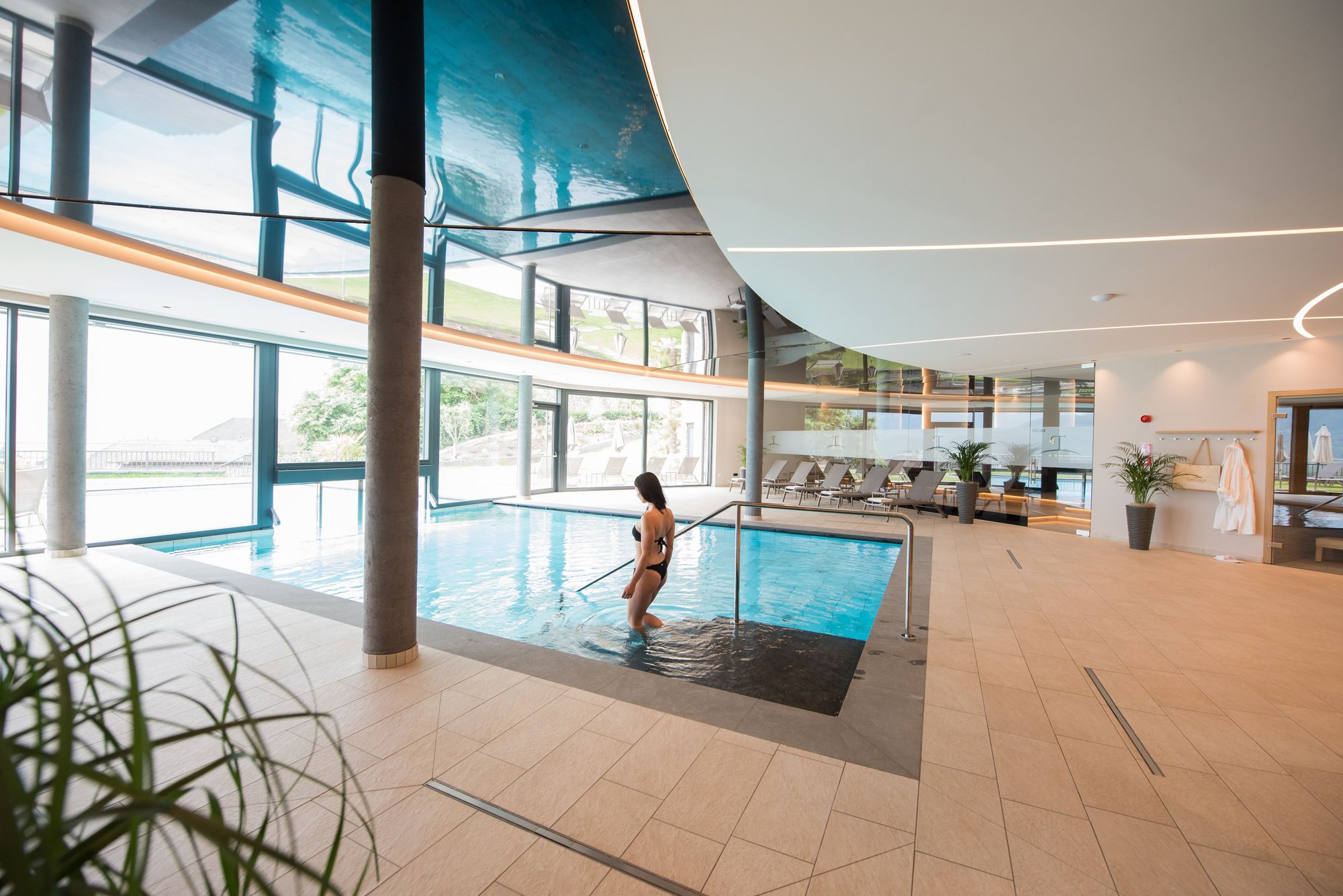 Frau betritt einen modernen Innenpool in einem hellen Wellnessbereich.