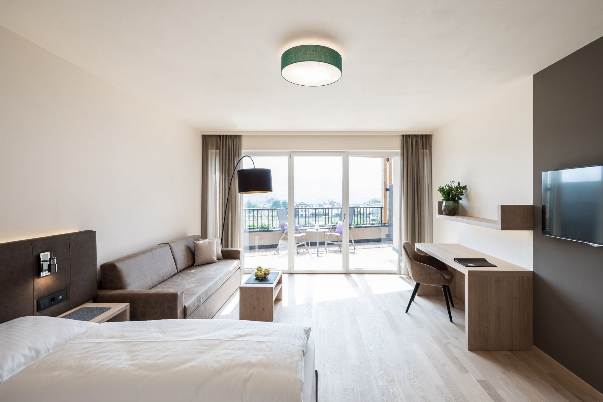 Helles Hotelzimmer mit Bett, Sofa, Schreibtisch und Balkonblick