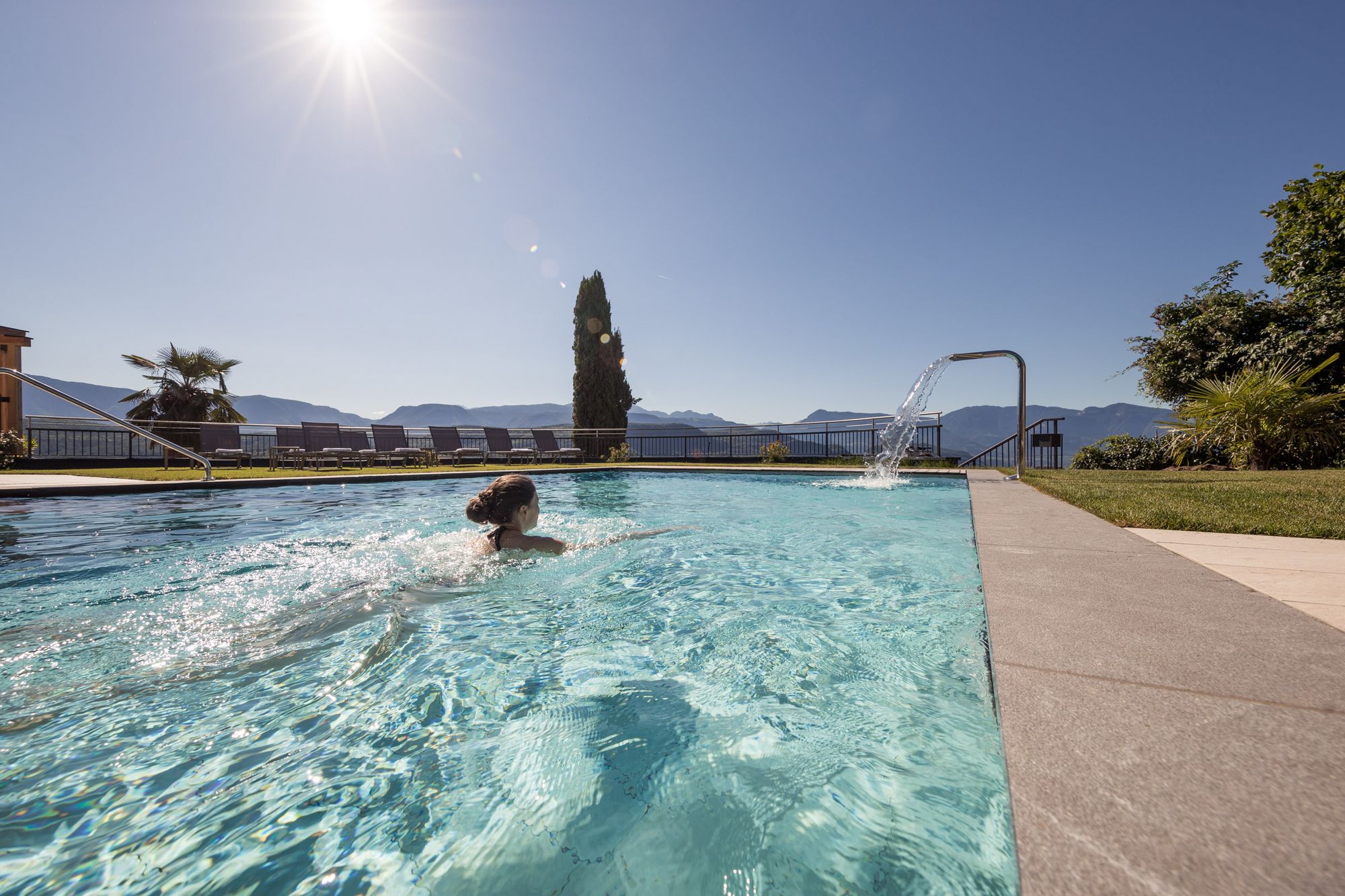 Frau schwimmt in einem Außenpool bei sonnigem Wetter mit Bergblick