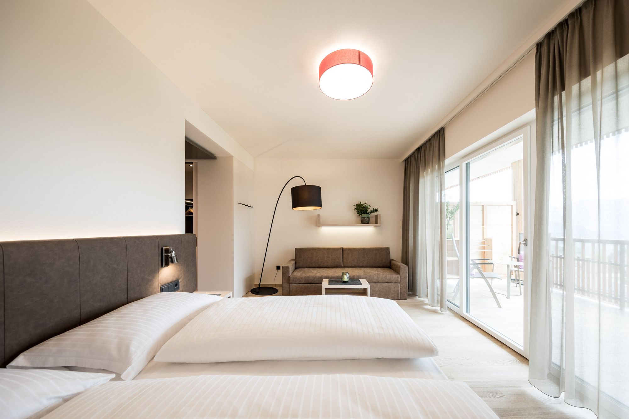 Modernes Hotelzimmer mit Bett, Sofa, Stehlampe und großer Fensterfront
