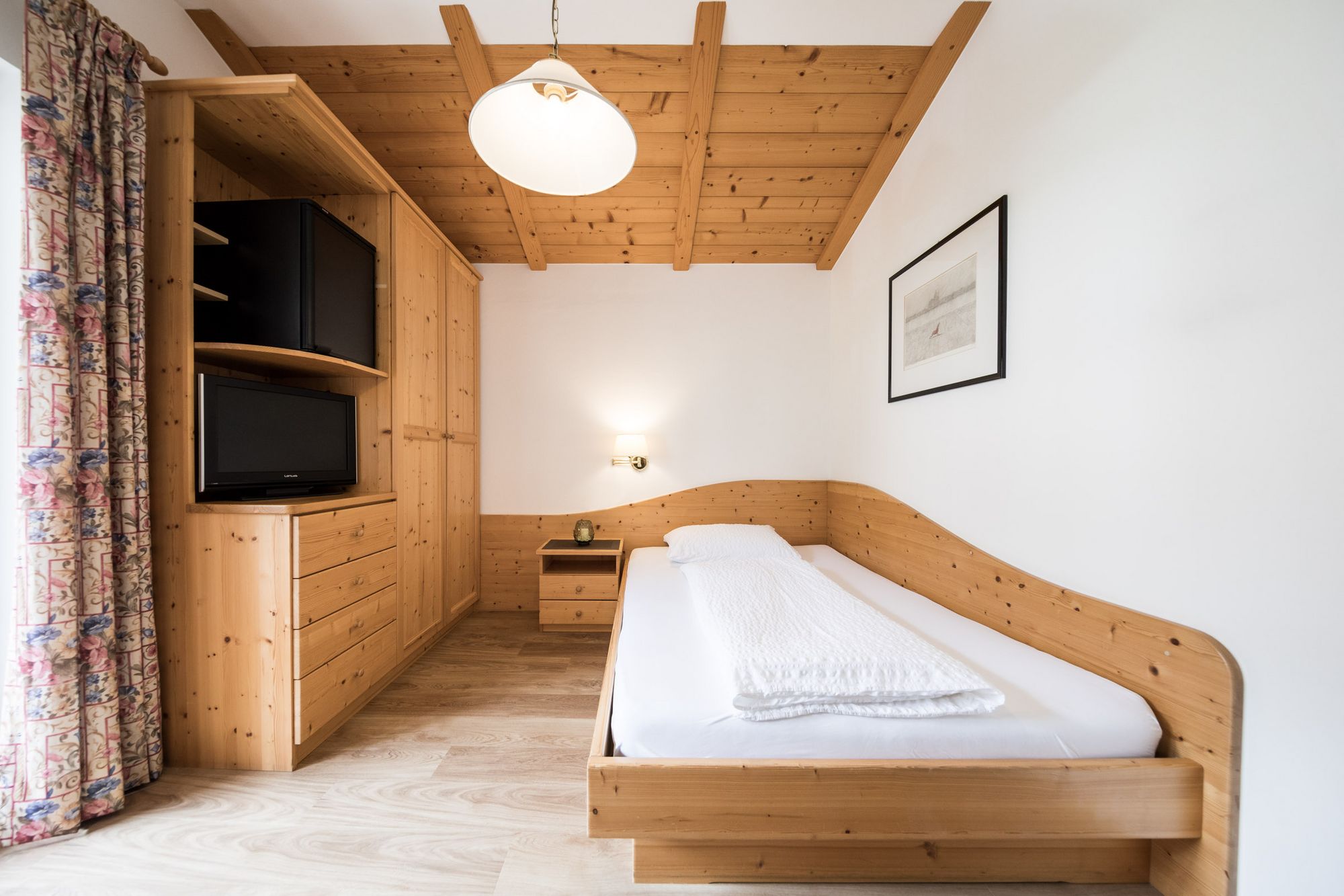 Kleines Schlafzimmer mit Holzmöbeln, Einzelbett und Fernseher.