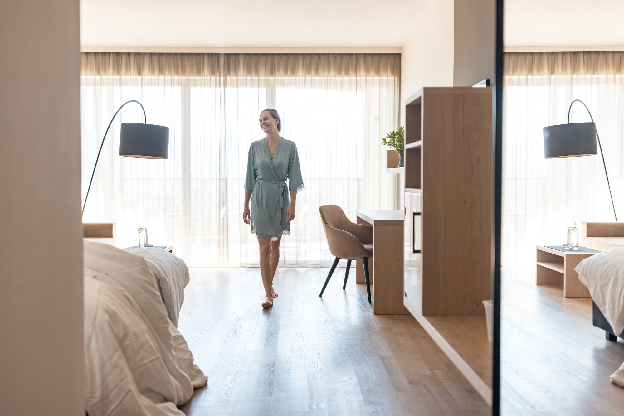 Frau im Bademantel geht durch ein helles Schlafzimmer mit Holzboden