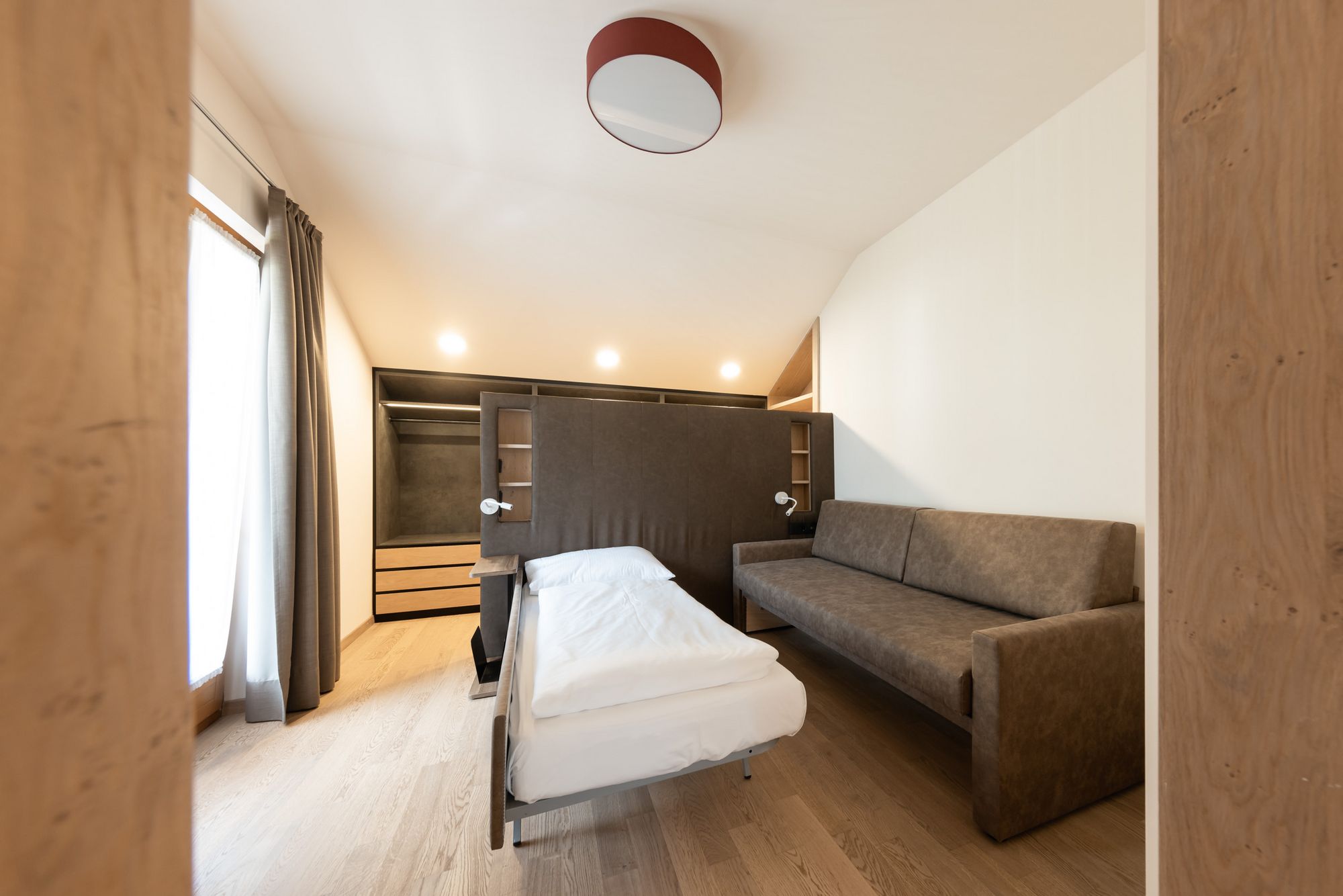 Kleines, modernes Schlafzimmer mit ausklappbarem Einzelbett und brauner Couch.