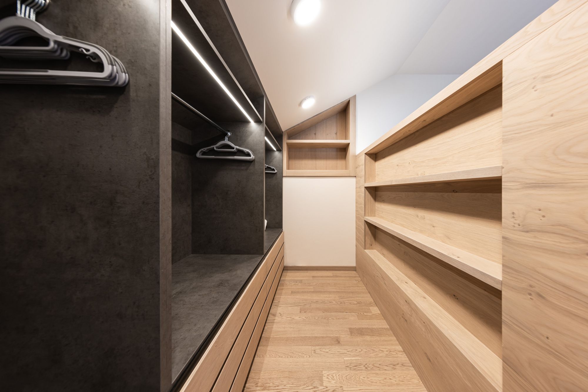 Moderner begehbarer Kleiderschrank mit Holzregalen und dunklen Fächern mit Kleiderbügeln.