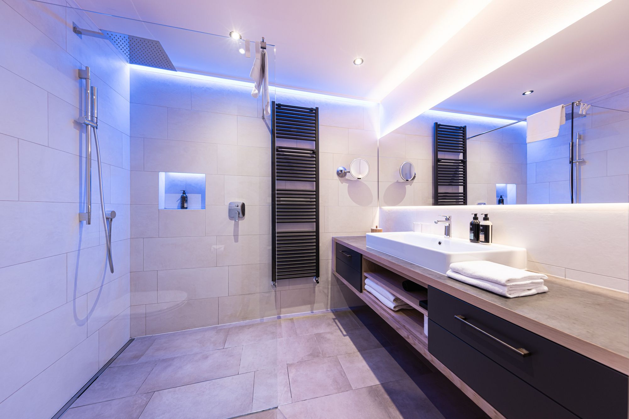 Modernes Badezimmer mit großer Dusche, Waschtisch und indirekter blauer Beleuchtung