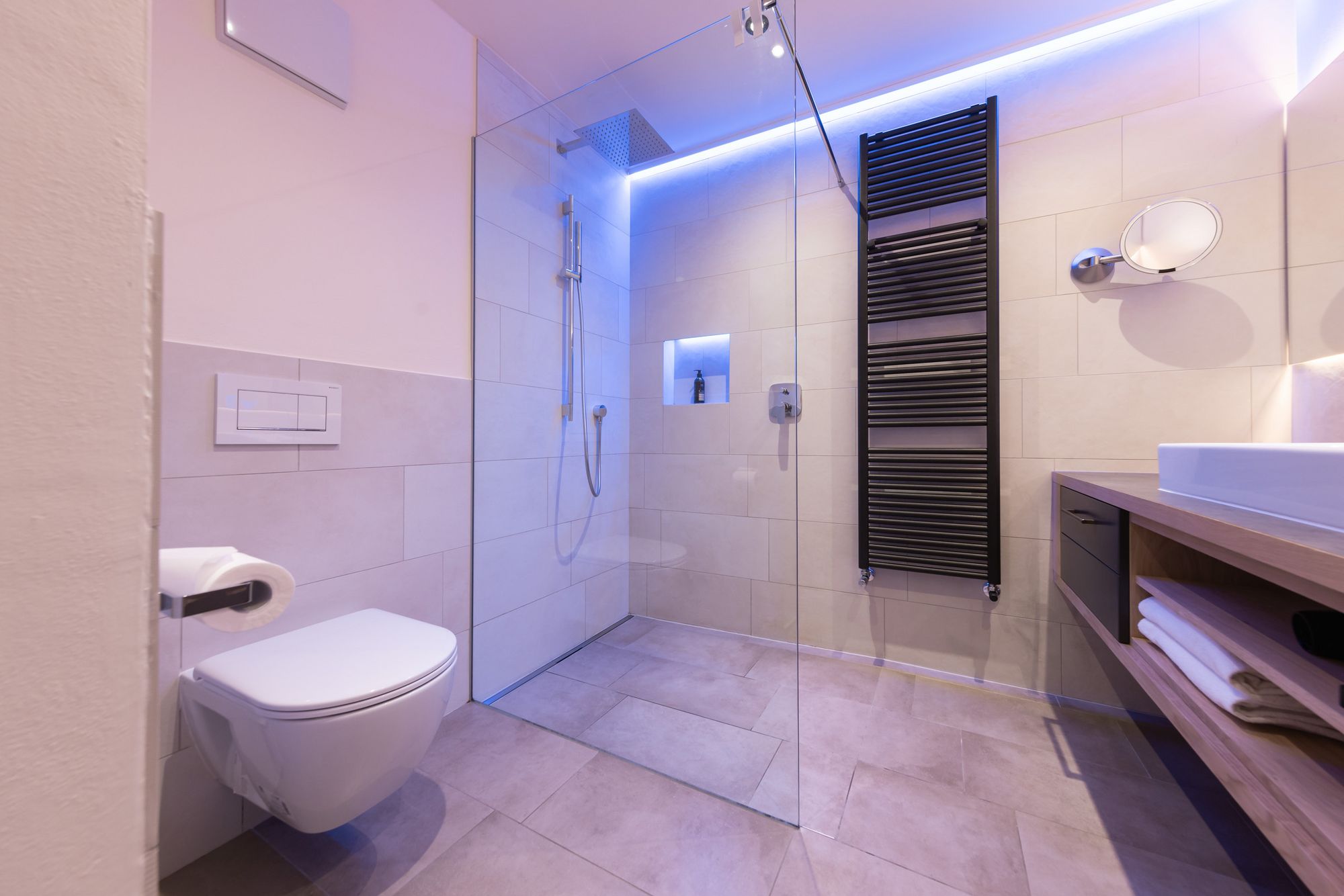 Moderner Badezimmer mit Dusche, Hänge-WC und beleuchtetem Spiegel.