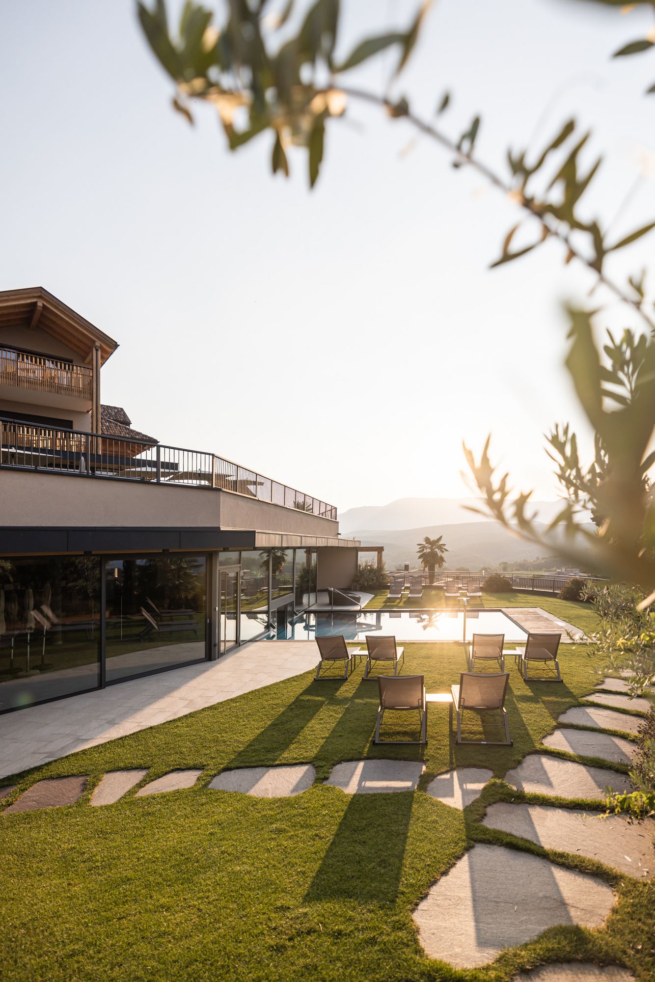 Sonnenuntergang über einer Terrasse mit Liegestühlen und Pool vor einem modernen Haus.