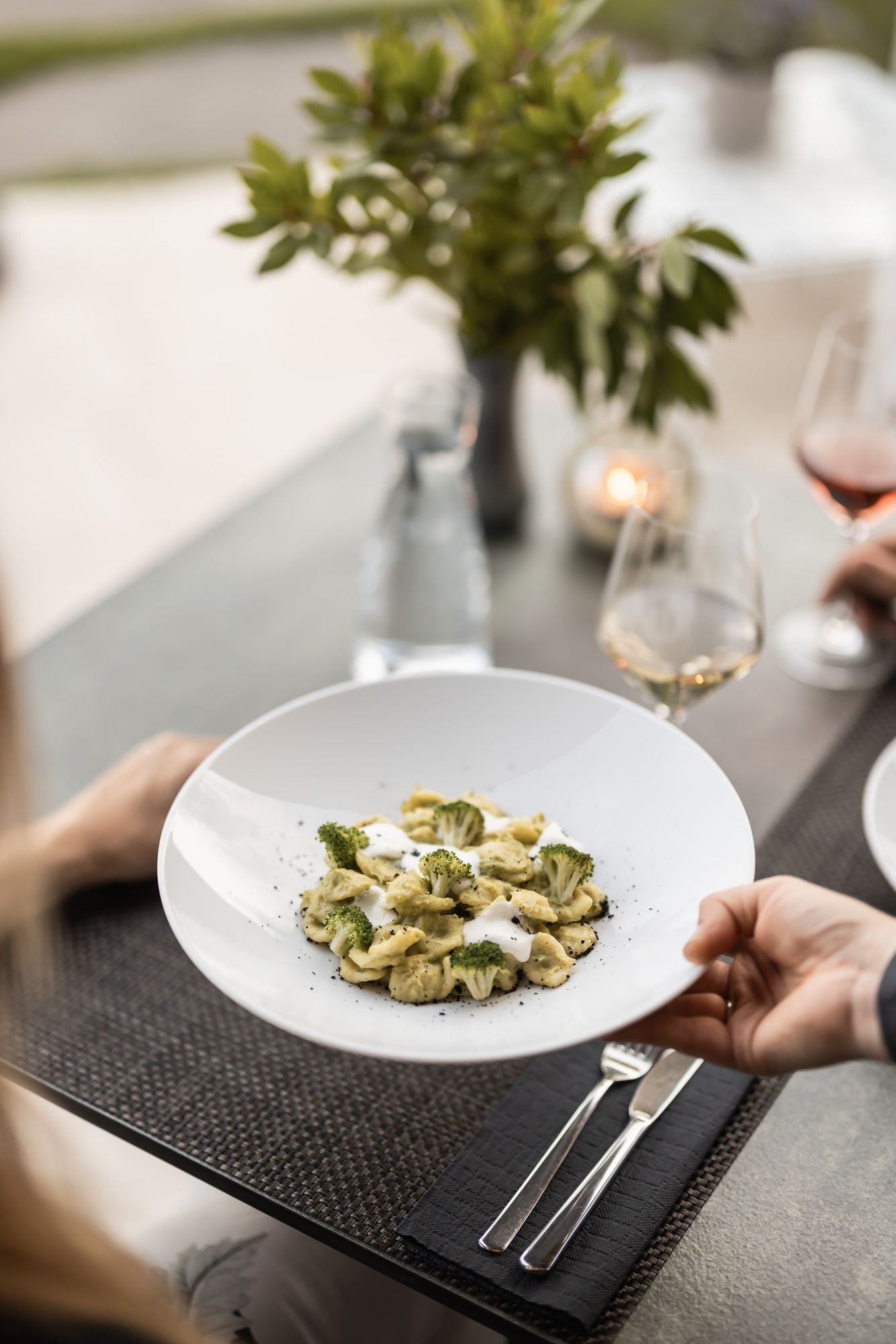 Person hält Teller mit Pasta und Brokkoli in einem Restaurant